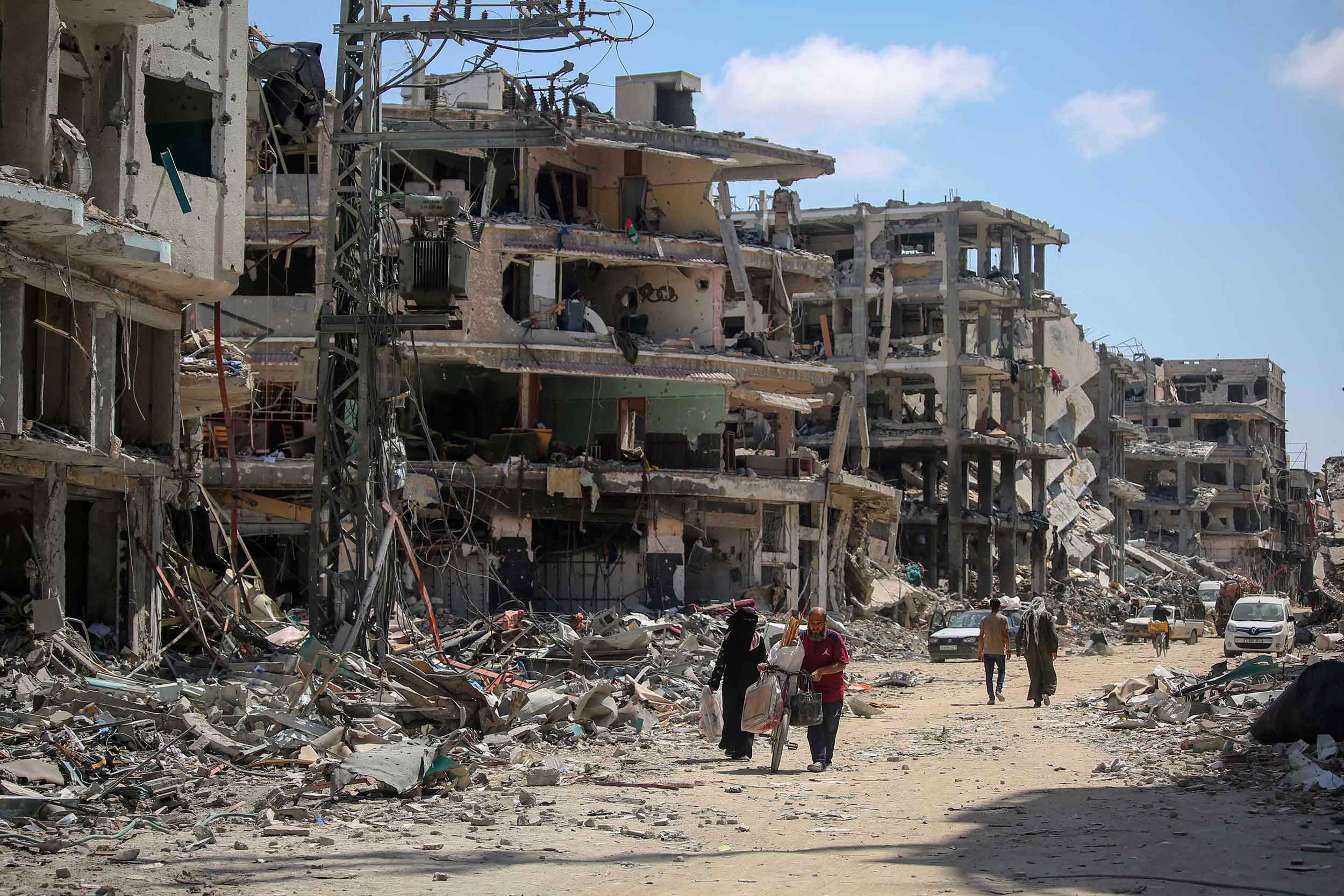 A man carries items on a bicycle while walking next to a woman as people remove possessions and inspect their homes following Israeli airstrikes on April 13, 2024 in Khan Yunis, Gaza. © Ahmad Hasaballah/Getty Images