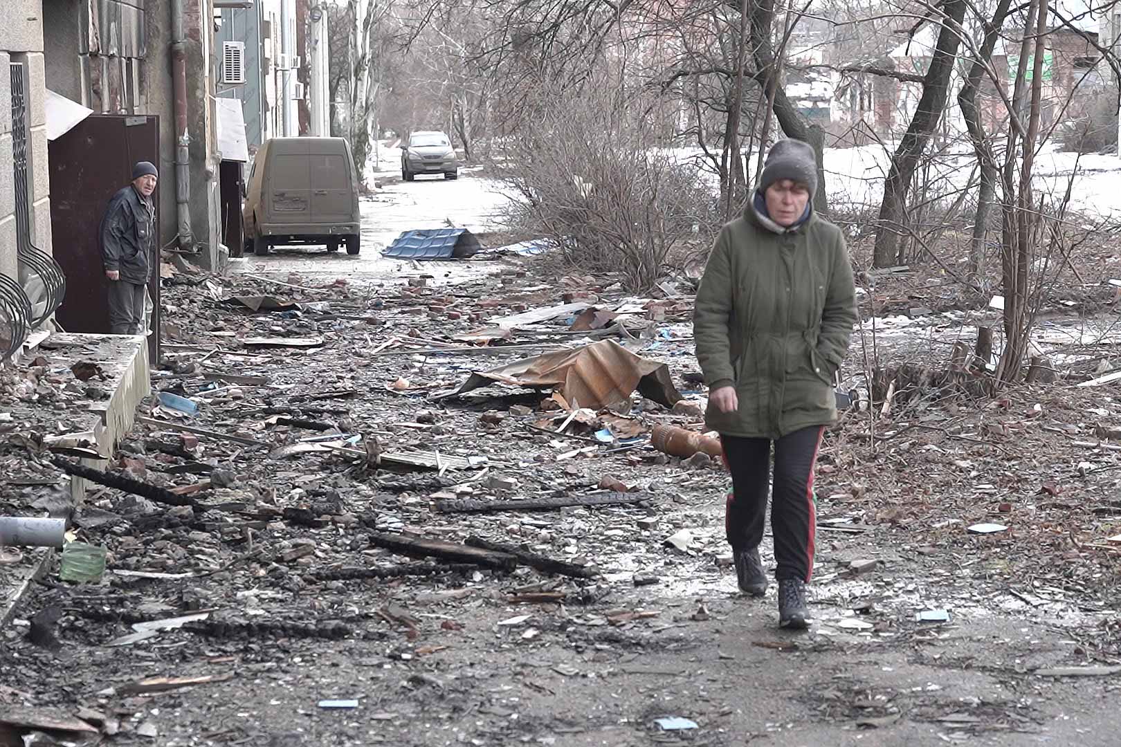 A woman walks amid charred-out buildings and rubble in Bakhmut; behind her a man stands at the door of one of the few shops still open in the town. Once home to about 73,000 people, Bakhmut is a ghost town with roughly 4,500 residents left, including 37 children. © Kolyan Pastyko